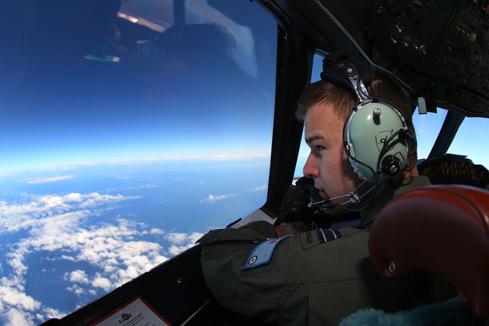 A pilot in an aircraft cockpit looking out at the ocean and clouds below.