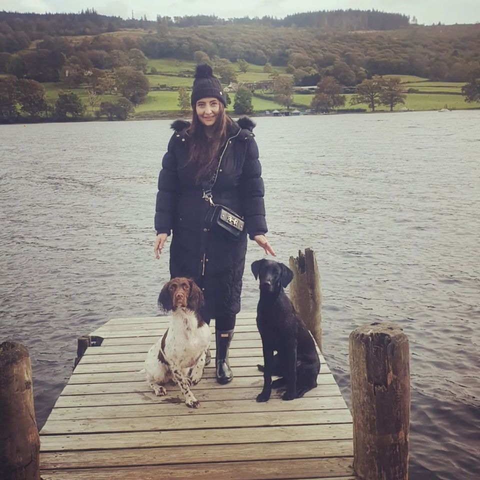 Woman with two dogs on a dock by a lake.