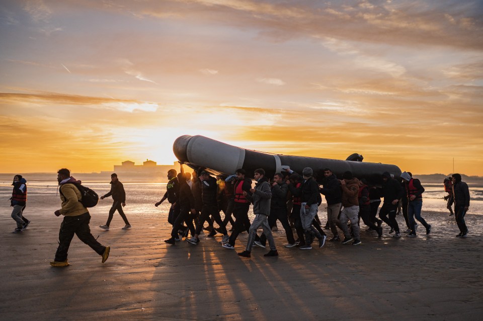 Migrants carry an inflatable boat as they prepare to leave France for Britain