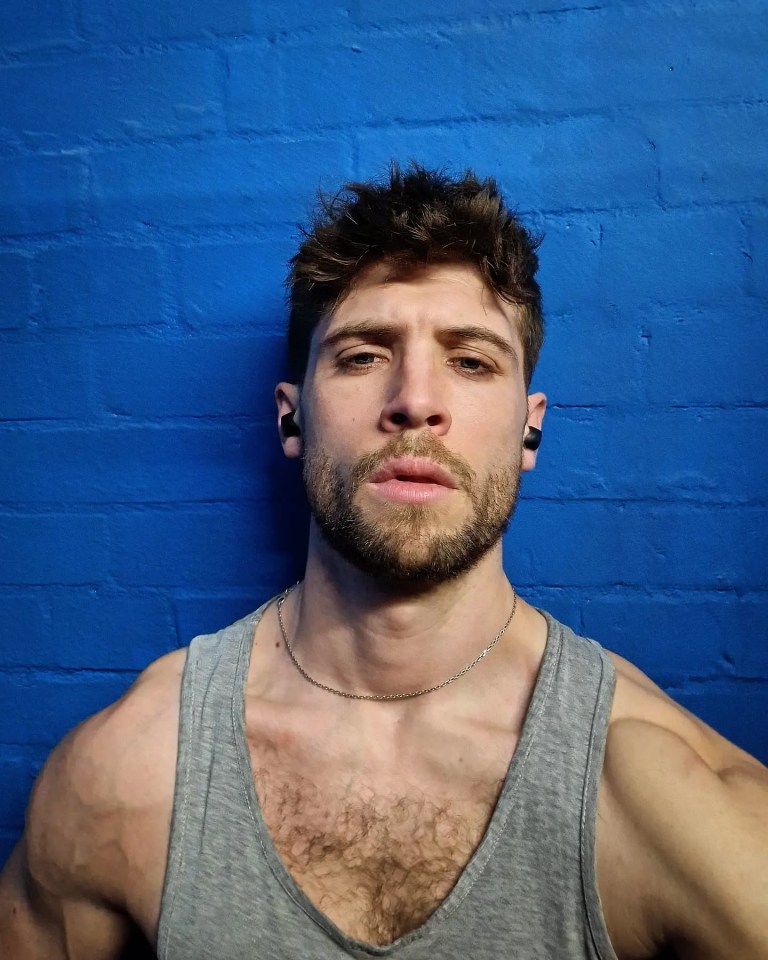 Close-up of Ned Porteous, wearing a gray tank top and earbuds, against a blue brick wall.