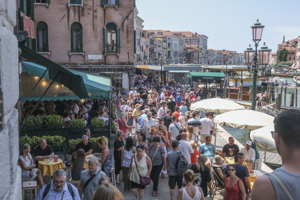 A crowded street scene in Venice, Italy, showing tourists near the Rialto Bridge.