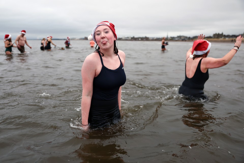 People in Santa hats participate in a charity swim in the sea.