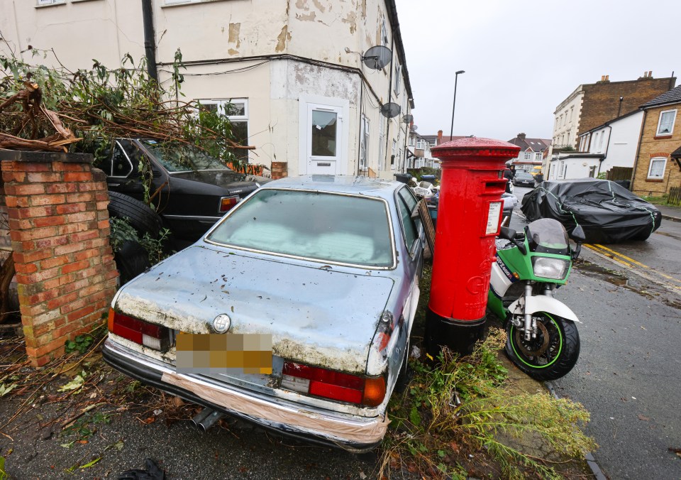 A rusty old BMW that is squeezed between a postbox and another BMW