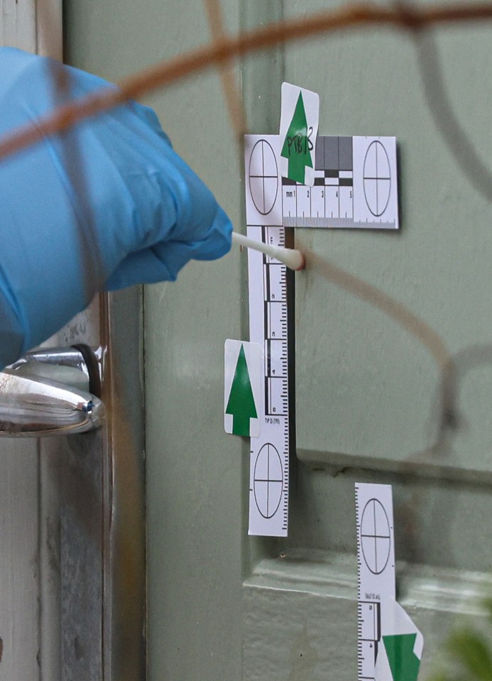 Forensic officer collecting a blood sample from a door at a crime scene.