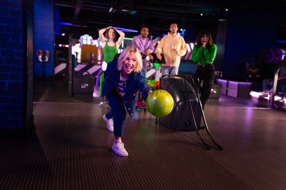 A woman bowls while her friends watch.