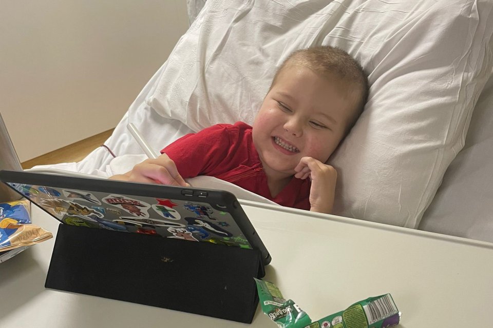 Smiling boy using tablet in hospital bed.