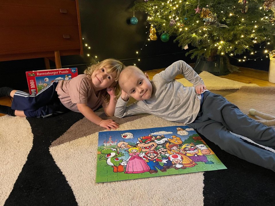 Two young boys lie on the floor near a Christmas tree, working on a Super Mario jigsaw puzzle.