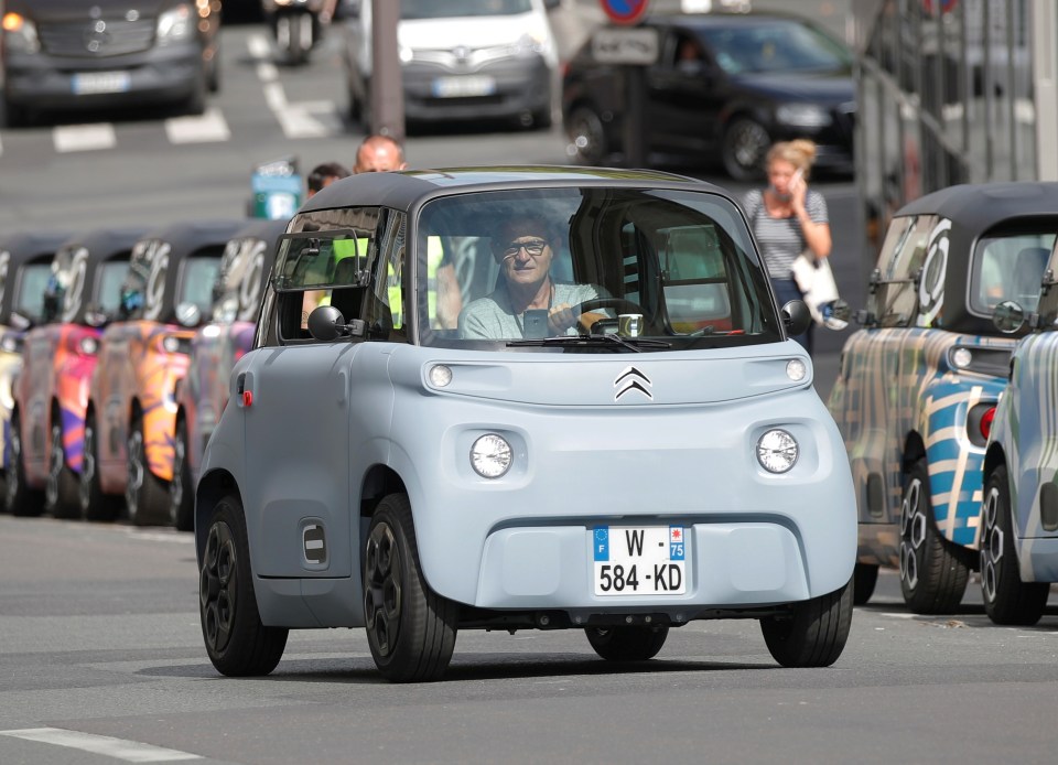 A light blue Citroen Ami electric car driving in Paris.