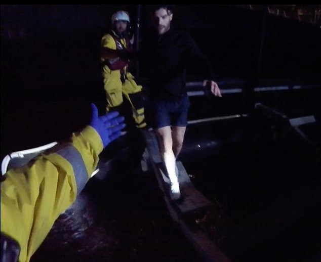 Rescue workers assisting a man onto a boat at night.