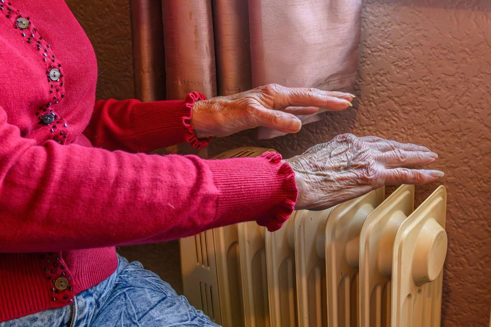 Elderly person's hands warming themselves on a radiator.