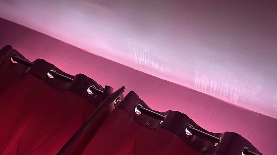 Close-up of maroon curtains hanging on a rod, with damage visible on the ceiling above.