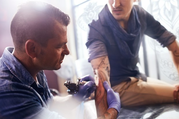 Tattoo artist applying a tattoo to a man's forearm.