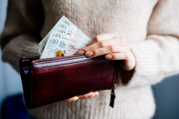 Woman placing British ten-pound notes in a wallet.