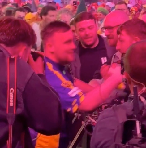 A man in a blue and yellow shirt is surrounded by people at a crowded event.