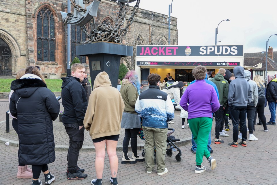 A long queue of people waiting to buy jacket potatoes from a food stall.