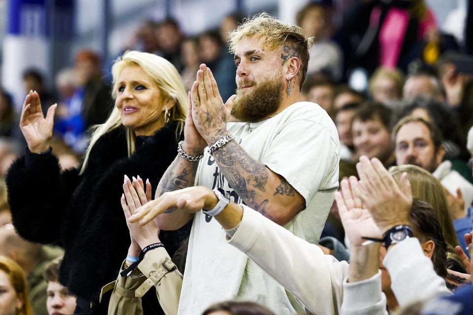 Jake Paul and a woman clap in the stands at a speed skating event.