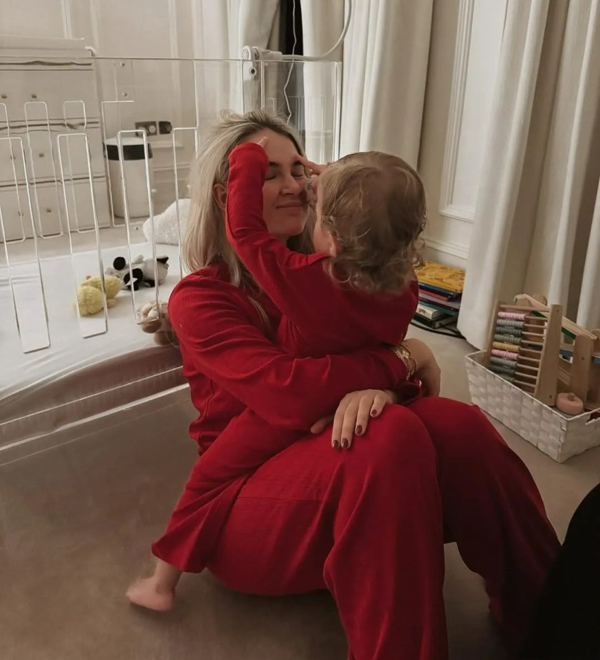 Woman in red pajamas cuddling her toddler near a crib.