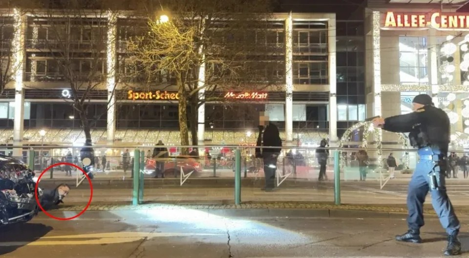 Taleb seen on the ground next to the car used to ram the market revellers as an officer points a gun at him