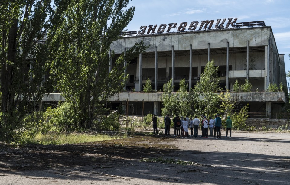 Tourists in Pripyat, Ukraine, near the Chernobyl Exclusion Zone, with the New Safe Confinement structure in the background.