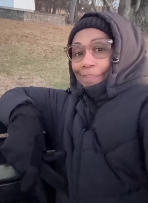 Trisha Goddard sits on a bench near a small lighthouse.