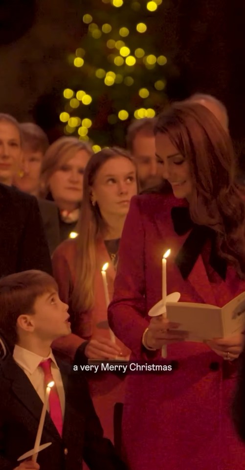 A woman in a red dress holds a candle and a book, while a young boy holds a candle next to her.  A Christmas tree is in the background.