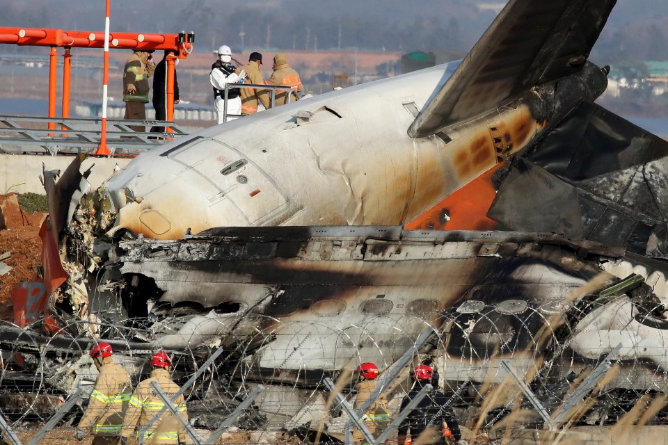 Burned wreckage of a passenger plane at an airport, with rescue workers present.