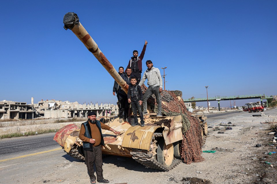 Syrians stand on the back of a tank on the Aleppo-Damascus International Highway