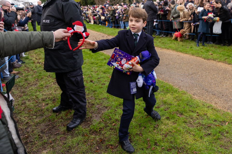 Prince Louis carrying Christmas presents and receiving a Santa headband.