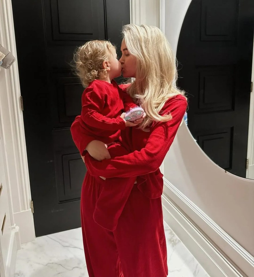 Woman in red pajamas kissing her child.