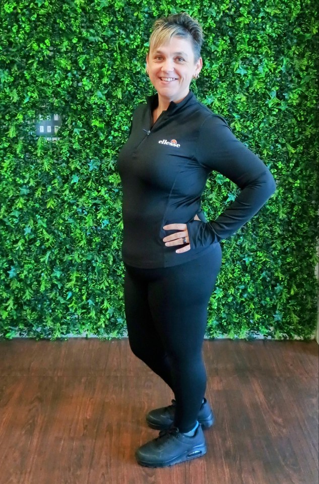 Woman in black athletic wear stands in front of a green wall.