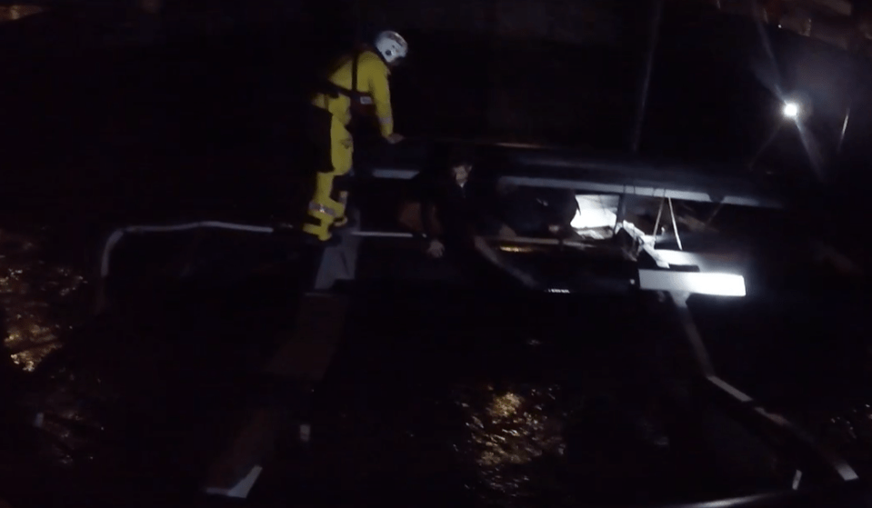 Rescue at night; a person in a yellow jacket assists people from a boat.