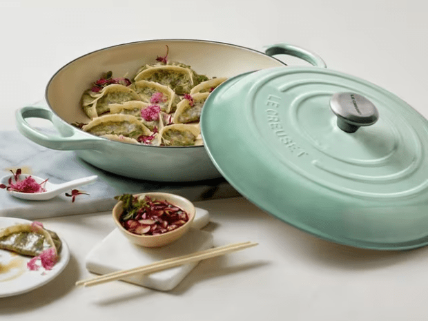 Green Le Creuset pot with dumplings and dipping sauce.