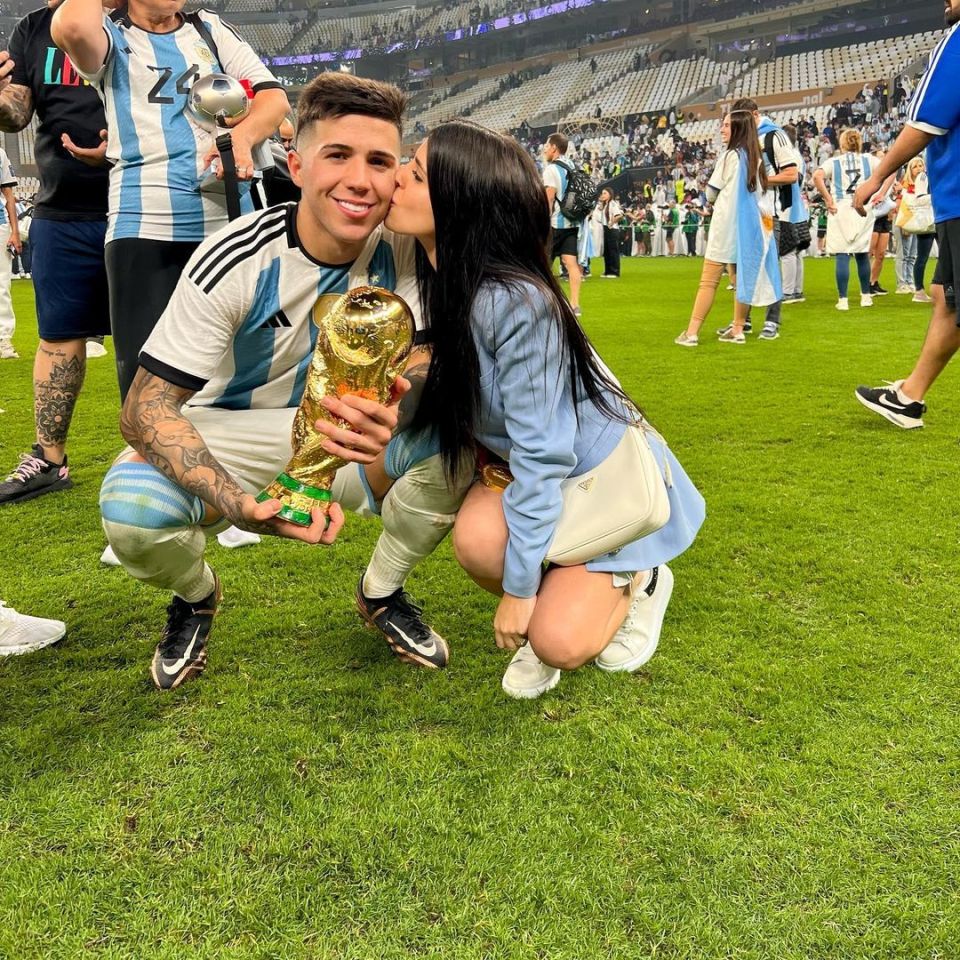 Soccer player holding the World Cup trophy, being kissed on the cheek by a woman.