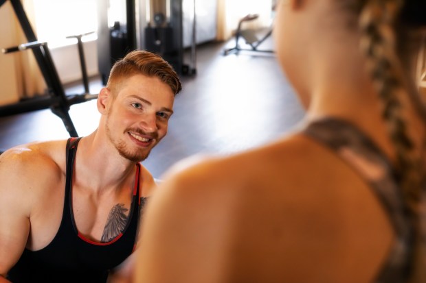 A young man smiles at a young woman in a gym.