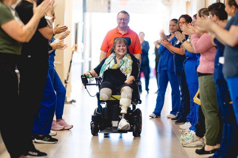 Lynne being wheeled out of hospital in front of medical staff and her partner