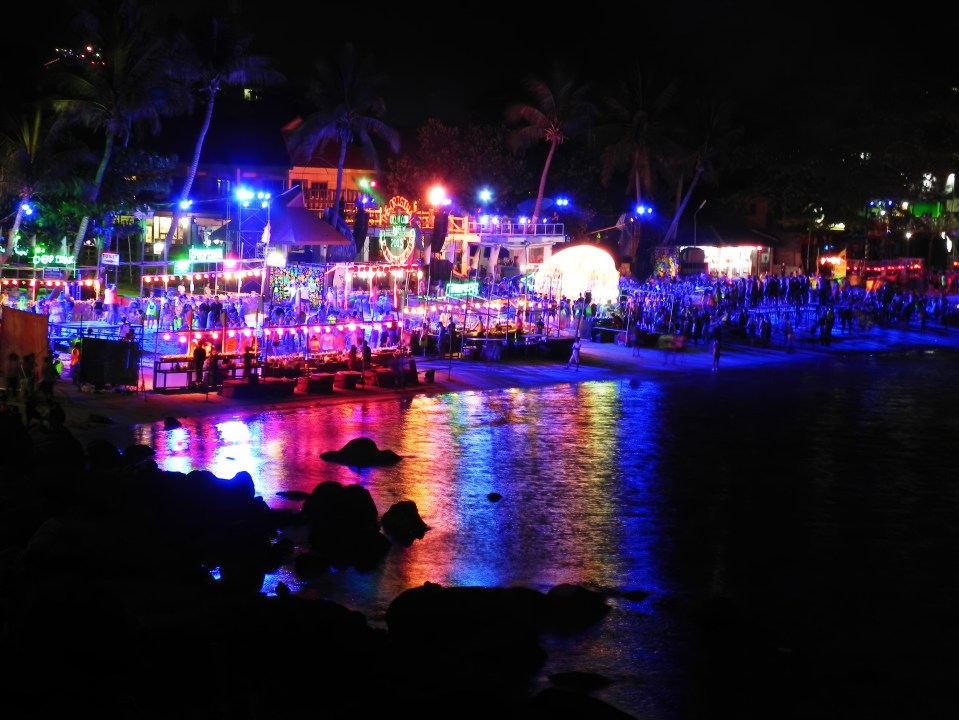 Nighttime beach party with colorful lights reflecting on the water.