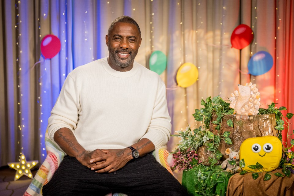 Idris Elba smiling while sitting in a chair.