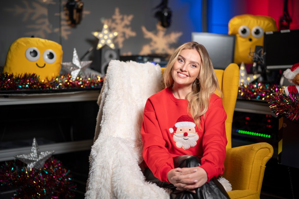 Woman in a red Santa sweater sits in a yellow armchair in a festive setting.