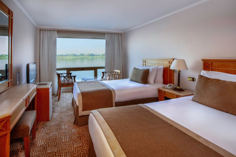 Nile cruise ship cabin with two beds and a river view.