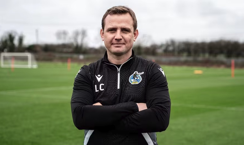 Headshot of a man in a black soccer coach's jacket.