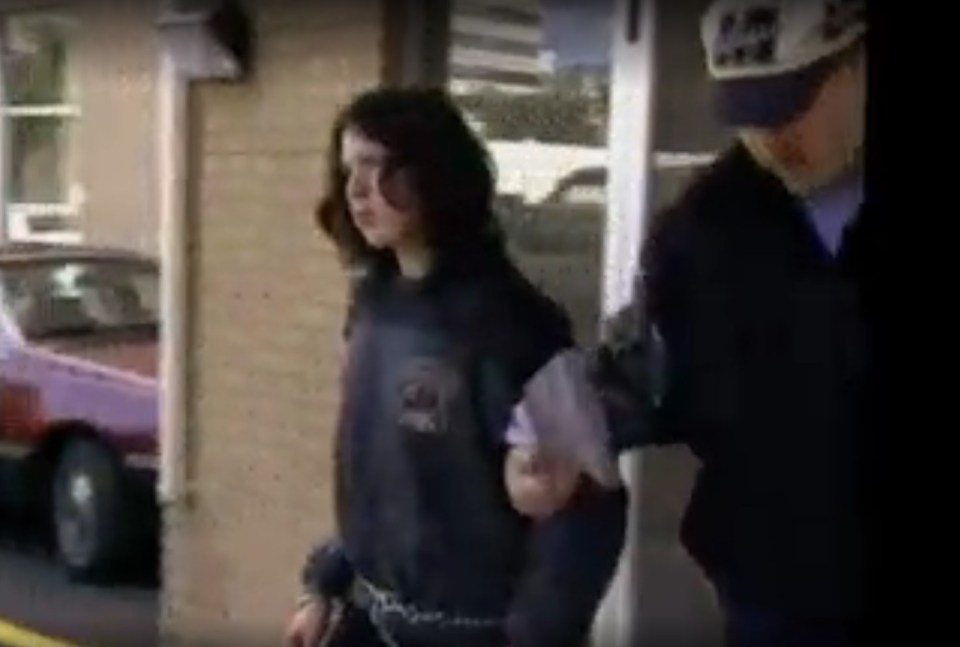 Sandy Charles in handcuffs, being escorted by police.