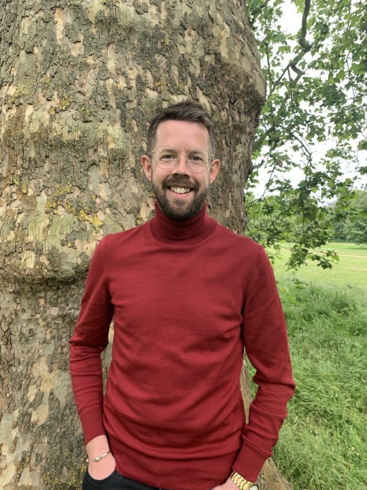 Man in red sweater standing by a tree.