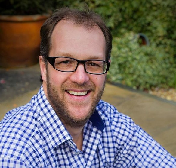 Headshot of a man wearing glasses and a blue and white gingham shirt.