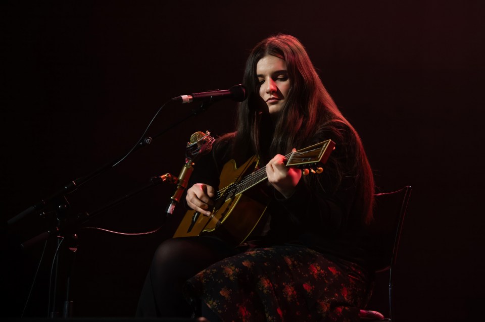 Woman playing acoustic guitar on stage.