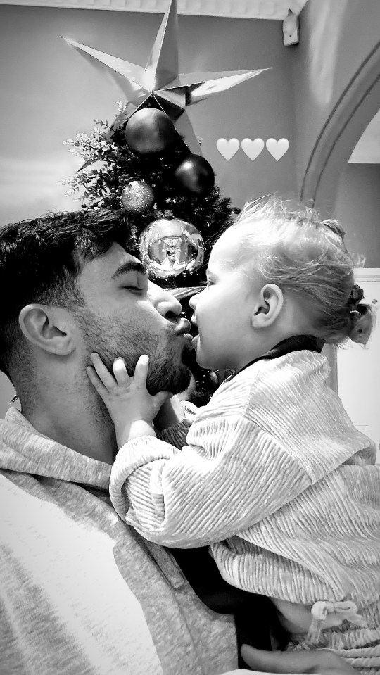 Black and white photo of a father and daughter kissing in front of a Christmas tree.