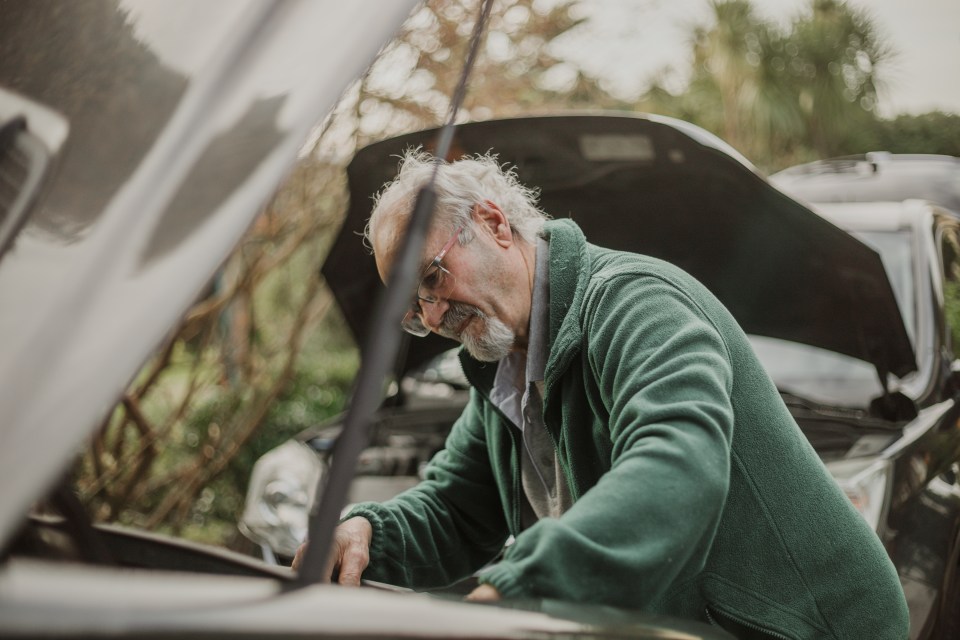 Senior man inspecting a broken-down car.