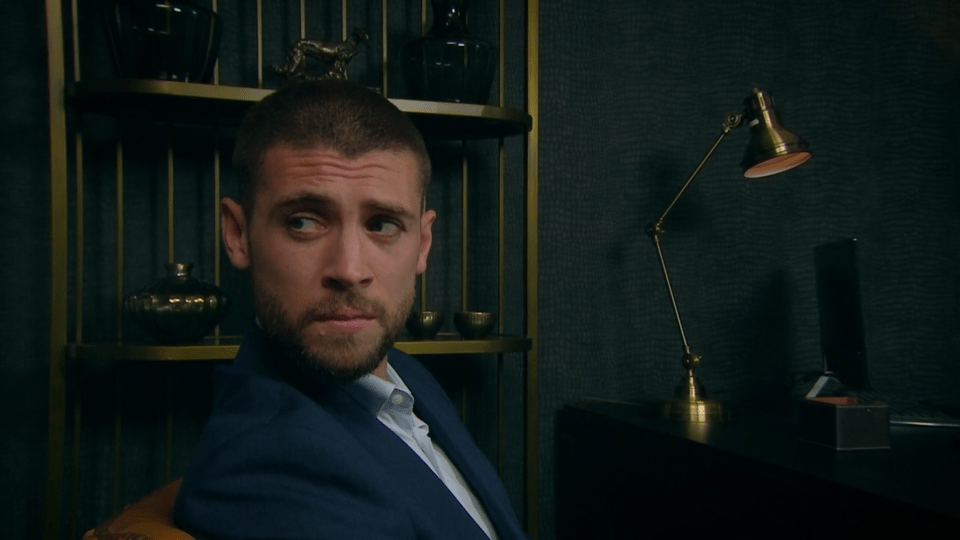 Man in a suit sits in a dimly lit office.