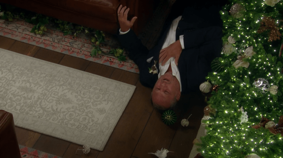 Man in suit lying on floor near Christmas tree.