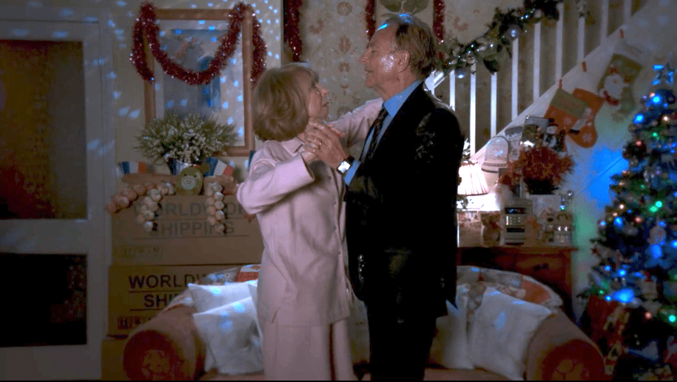 A couple slow dances in a Christmas-decorated living room.