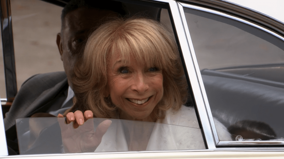 A woman smiles and waves from a car window.